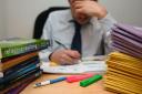 A school teacher looking stressed next to piles of classroom books (PA)