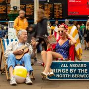 Eric Wales, musician and founder of Fringe by the Sea, and North Berwick-based artist Bonzo-Art take a moment out to celebrate the spirit of the Fringe at Edinburgh Waverley Station, encouraging passengers to head to North Berwick for Fringe by the Sea.
