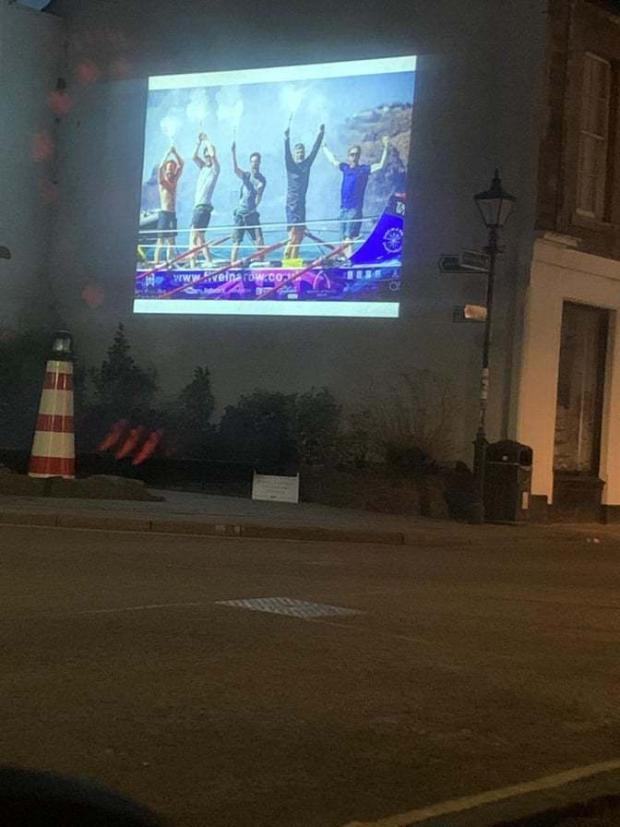 East Lothian Courier: A projection of the moment the team arrived at the finish line has been beamed onto the side of a building on North Berwick High Street to celebrate their achievement