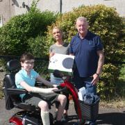 Alex Brown, owner of Ideal Flooring Solutions in Musselburgh, presents a mobility scooter and Xbox to Reece Dodds. Looking on is Reece's mum Pauline